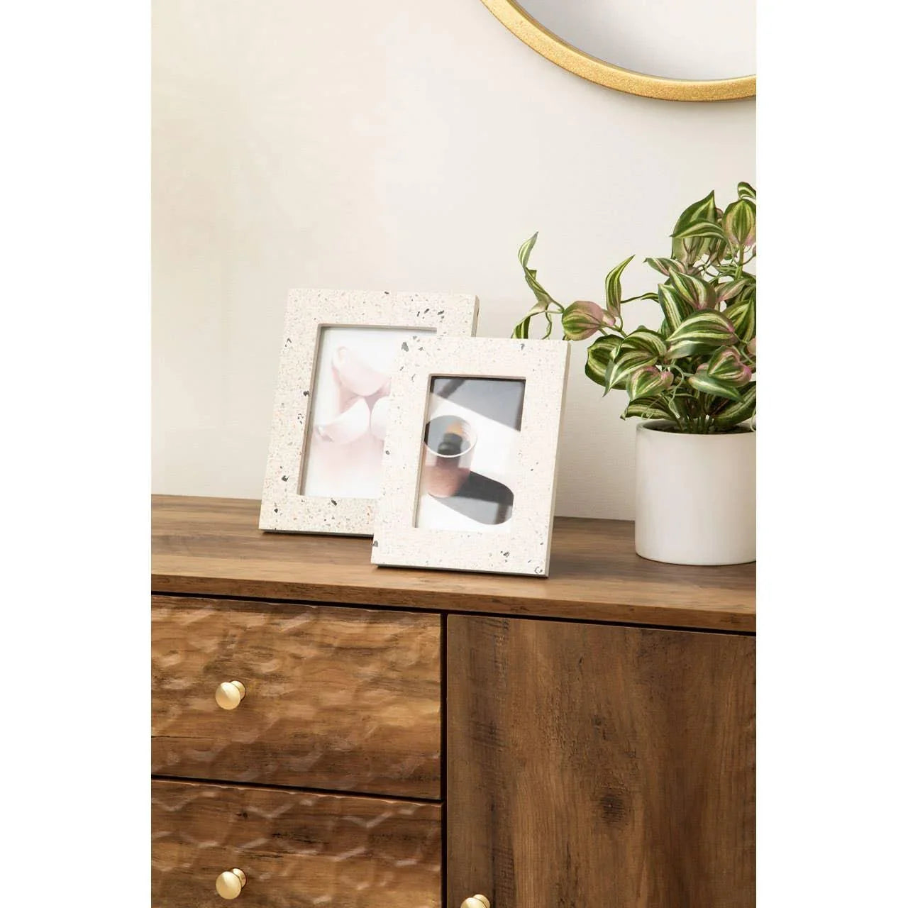 Terrazzo photo frames on wooden sideboard with potted plant and mirror