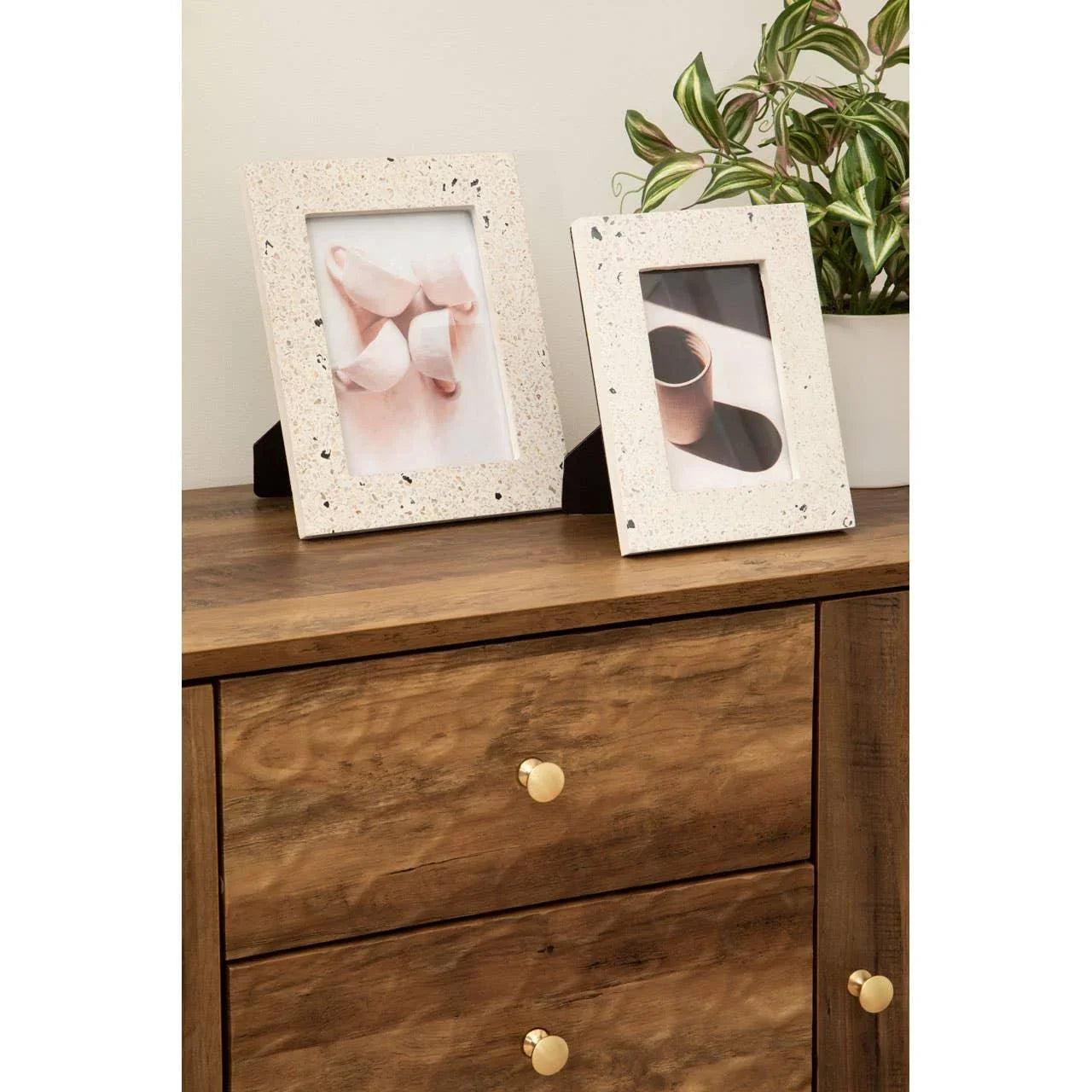 Wooden chest of drawers with gold knobs, terrazzo photo frames, and potted plant