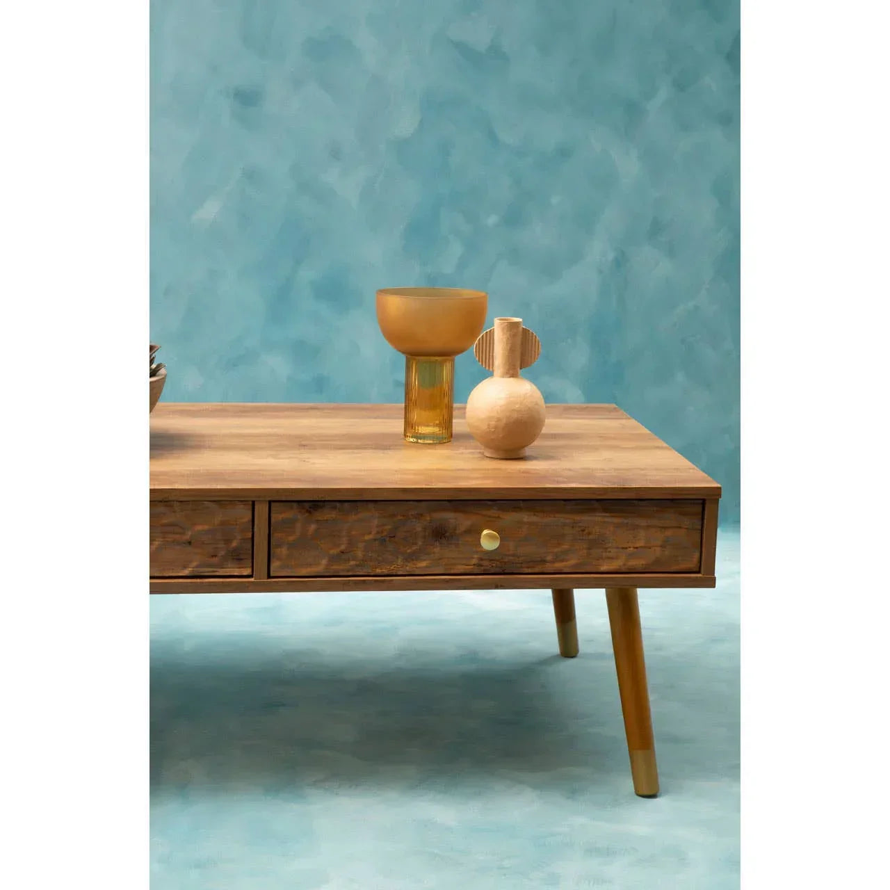 Wooden coffee table with drawer, gold knob, and decorative vases against blue wall