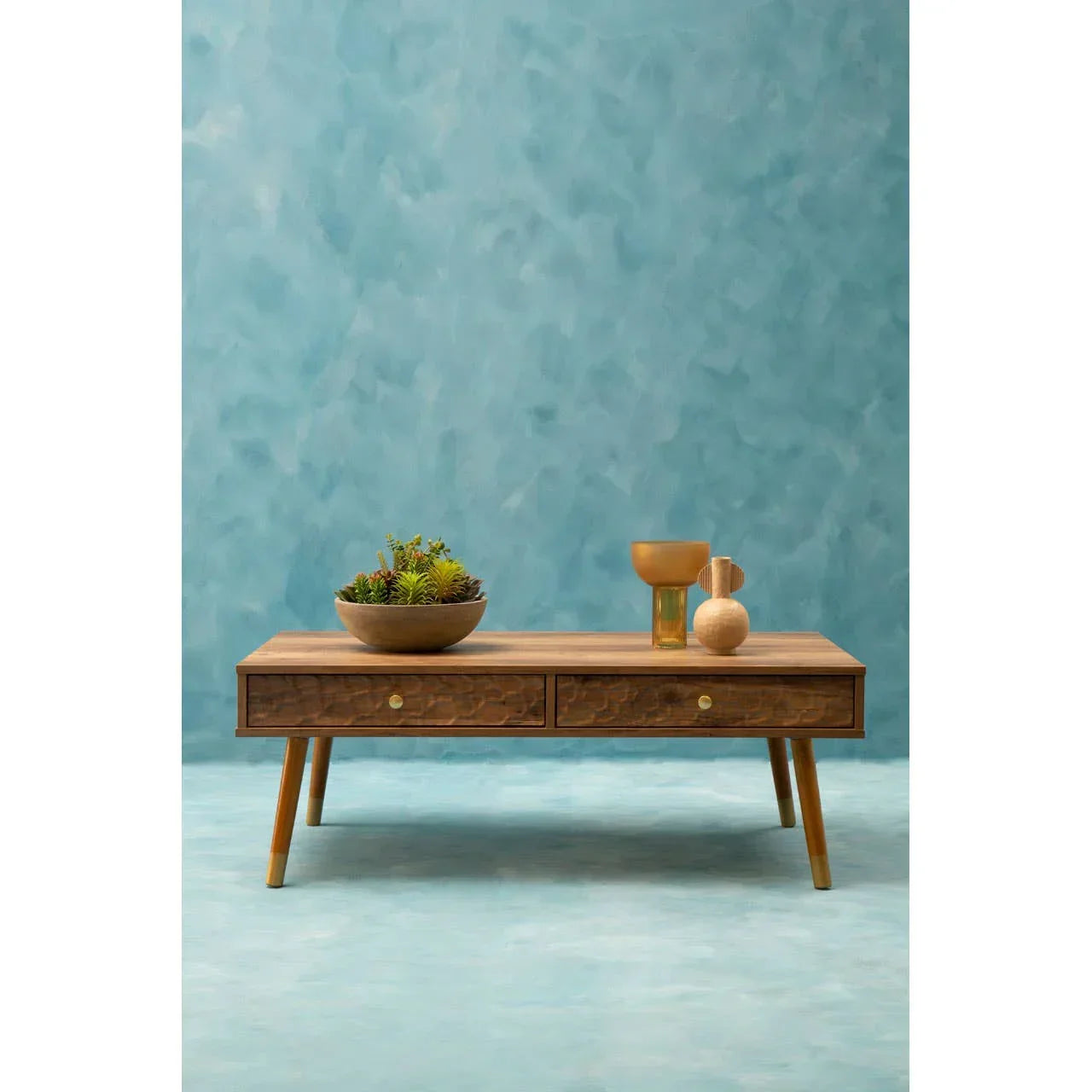 Wood coffee table with two drawers, decorative bowl and vases against blue wall