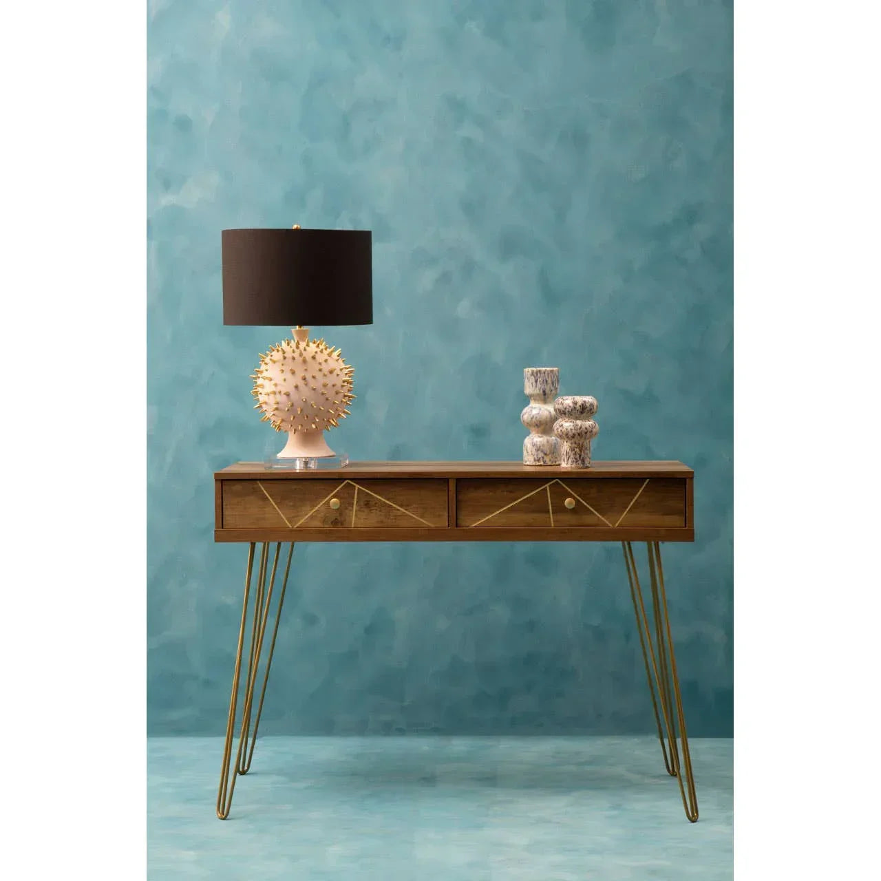 Wood console table with gold legs, two drawers, lamp, and decorative vases against blue wall