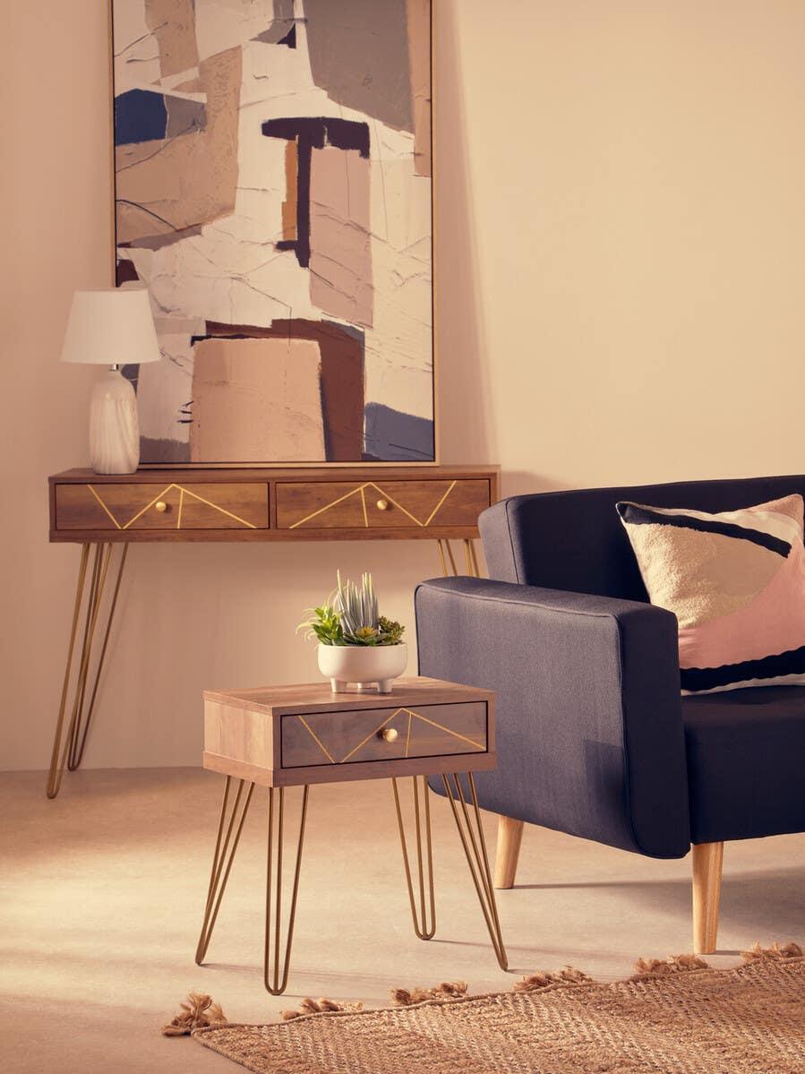 Modern wooden side table with gold hairpin legs beside navy sofa and geometric wall art
