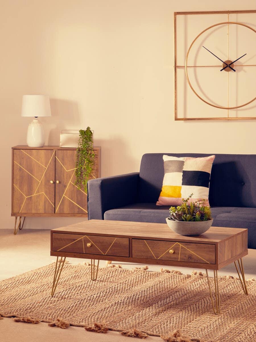 Modern wood coffee table with gold legs on woven rug, navy sofa and geometric cushion behind