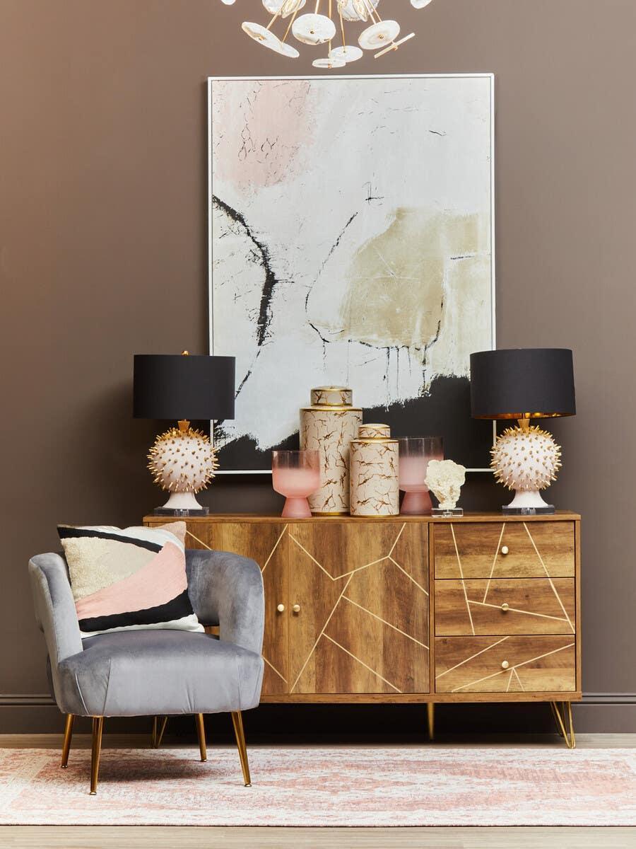 Wooden sideboard with geometric gold inlay, grey accent chair, decorative lamps and vases