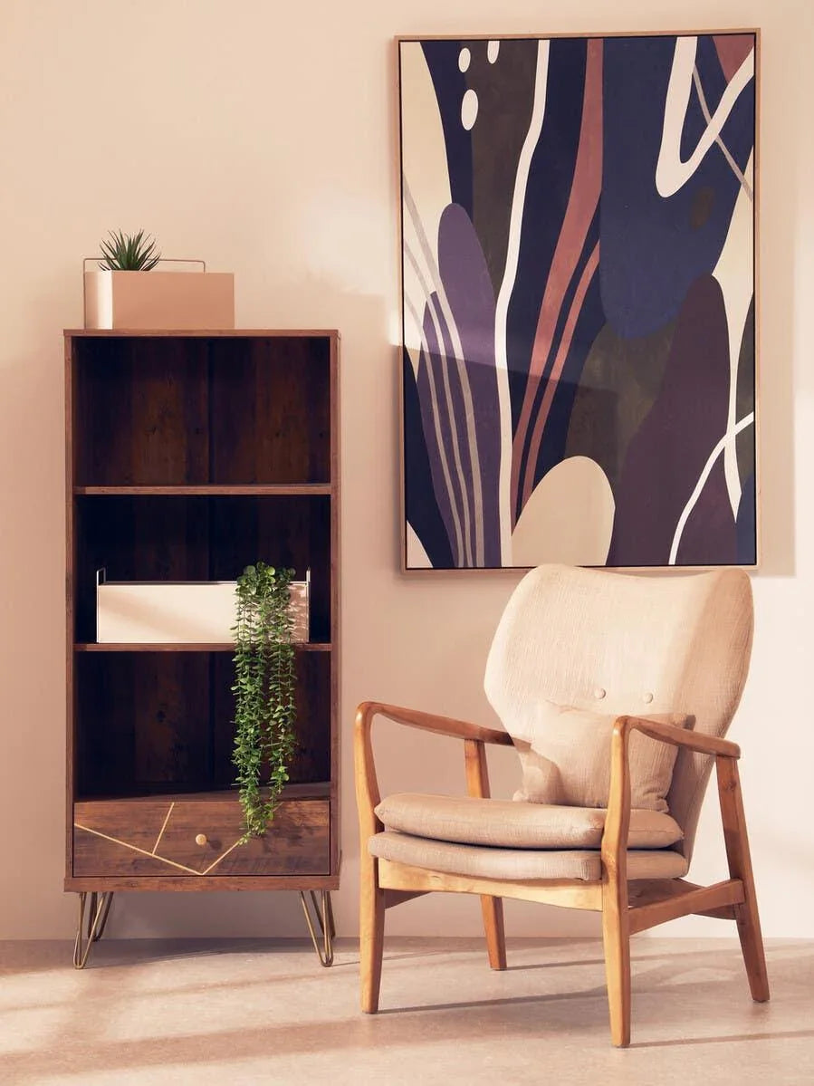 Wooden armchair with cream cushions beside a modern bookcase and abstract wall art