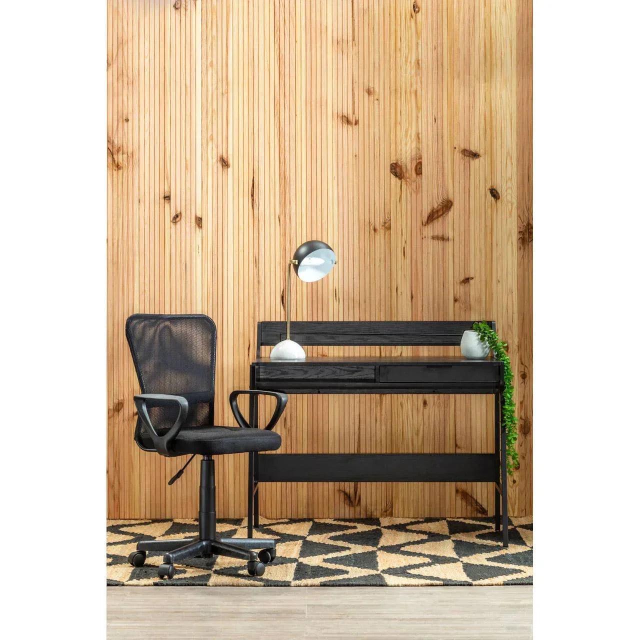 Black office desk with drawers and black mesh swivel chair on patterned rug