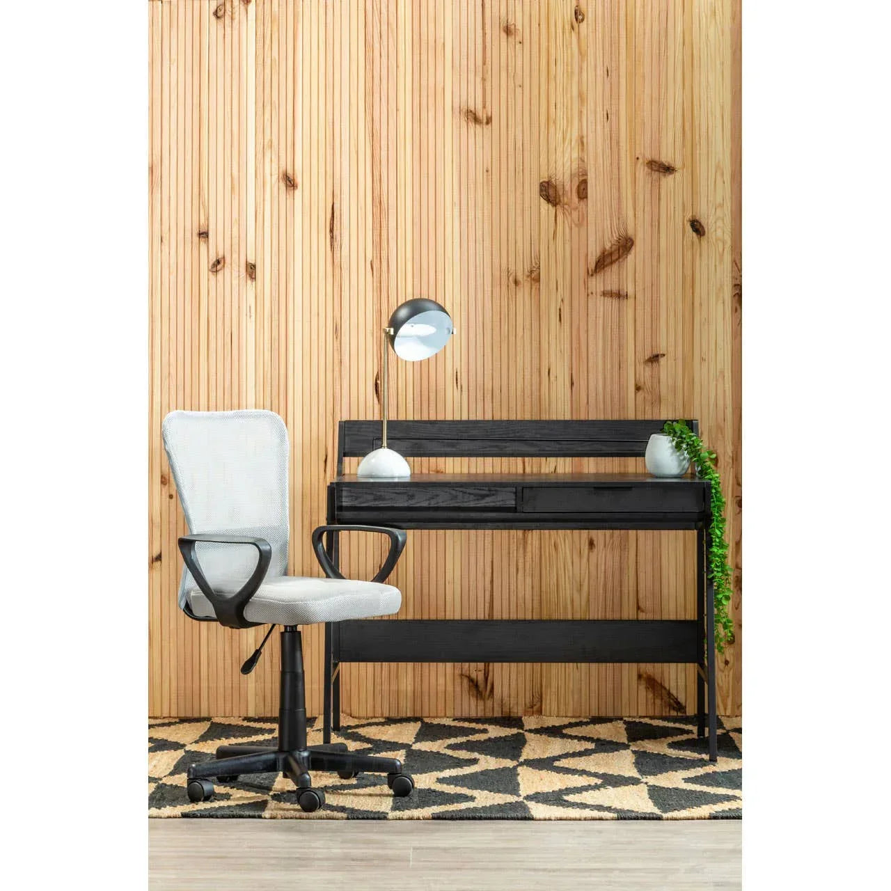 Black wooden home office desk with drawers and grey swivel chair on patterned rug