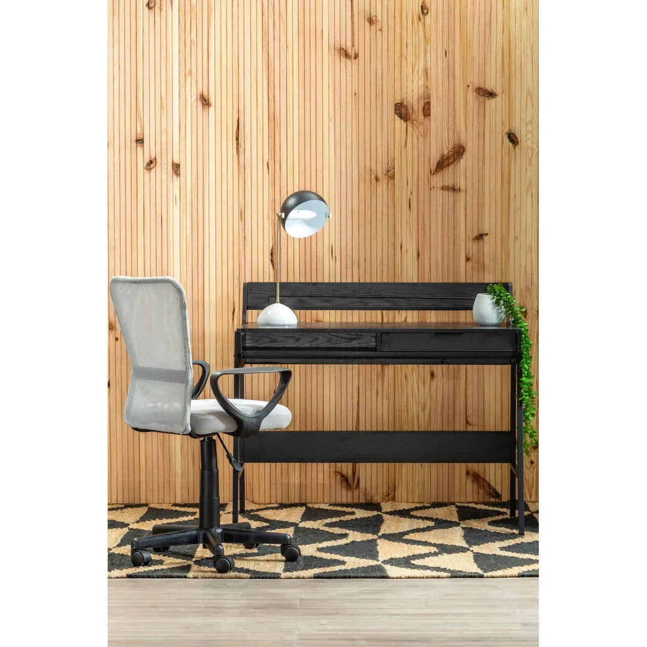Black wooden desk with drawers and modern grey office chair on geometric rug