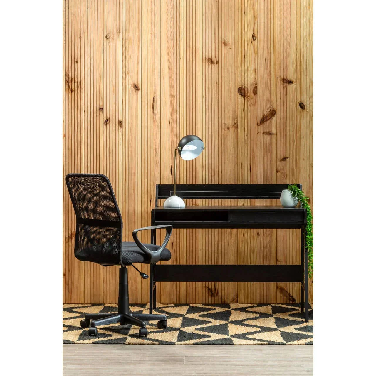 Black mesh office chair with modern black desk and lamp against wooden wall