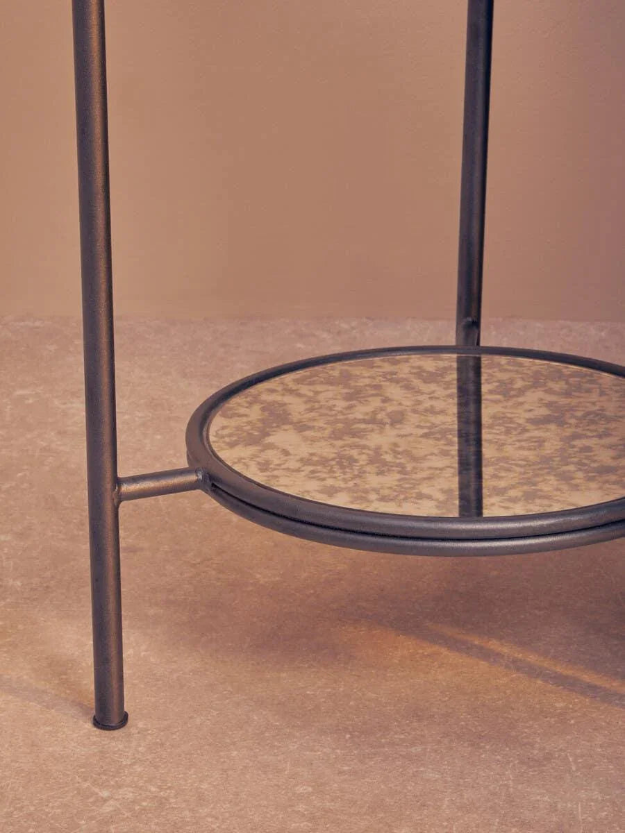 Round metal side table with mottled glass lower shelf on stone tile floor