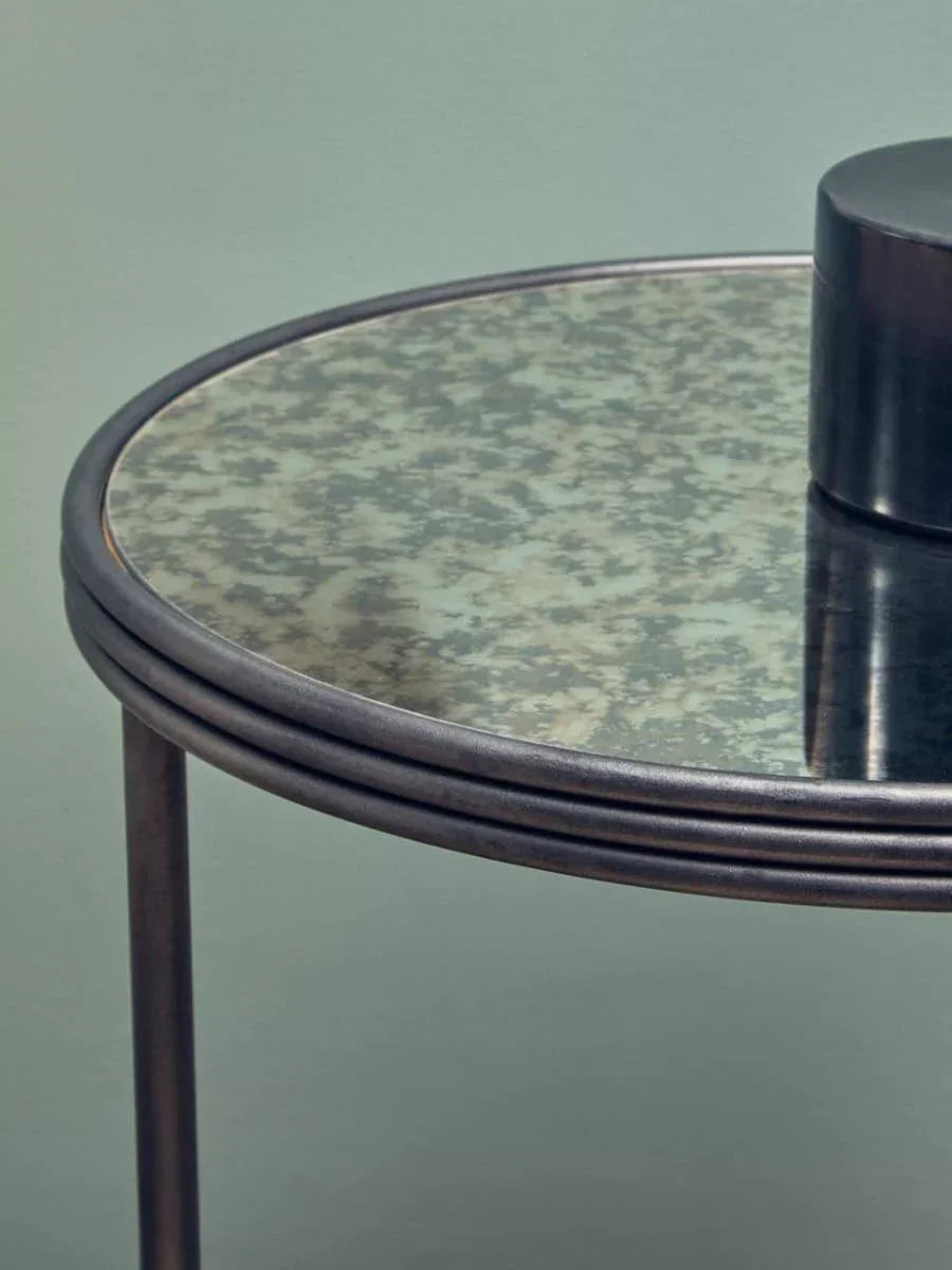 Round side table with antique mirrored glass top and metal frame, close-up view
