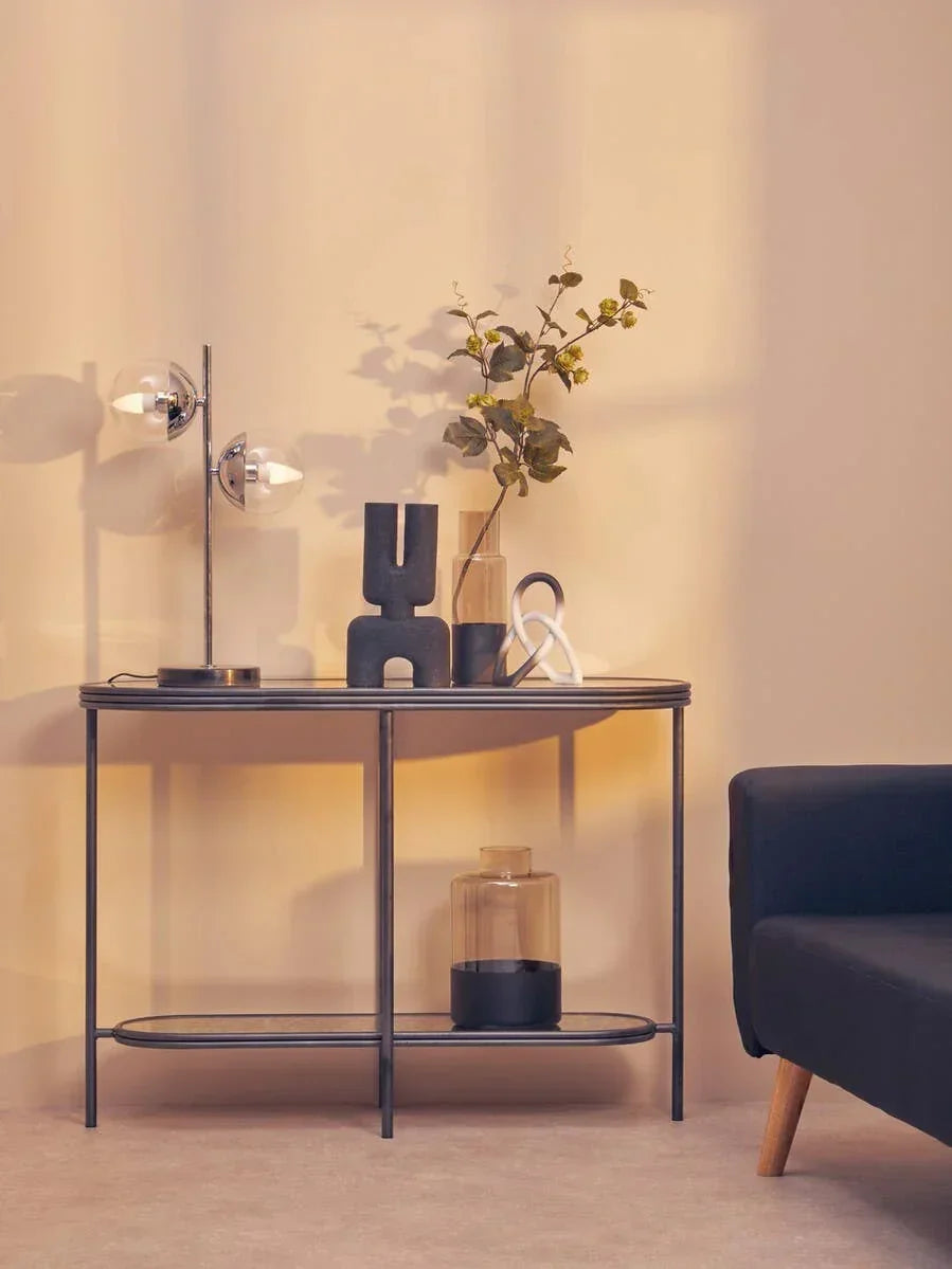 Modern black metal console table with glass top, decorative lamp, vases, and sofa corner