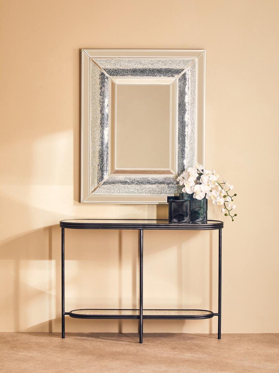 Rectangular wall mirror with textured silver frame above black metal console table in hallway