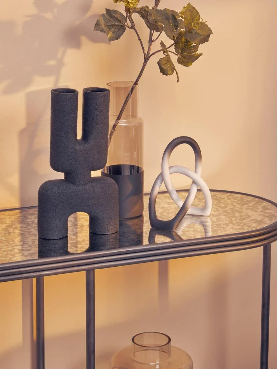 Black ceramic vase, glass vase with green foliage, and sculptural knot decor on console table