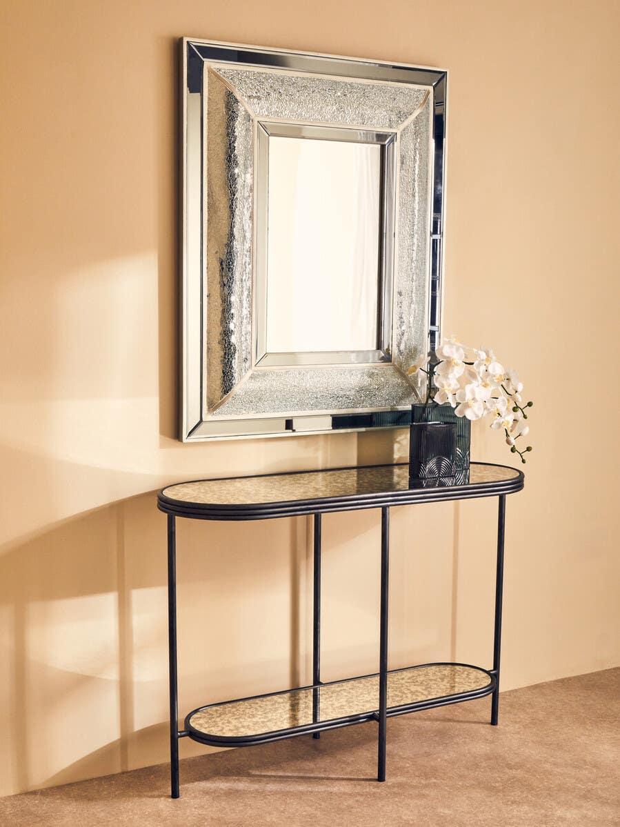 Mirrored console table with black frame and glass top below large rectangular wall mirror