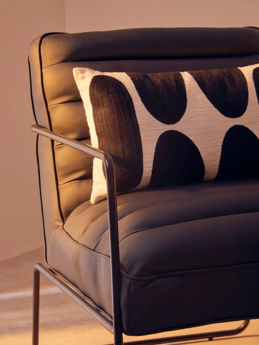 Black leather armchair with metal frame and geometric cushion in warm lighting