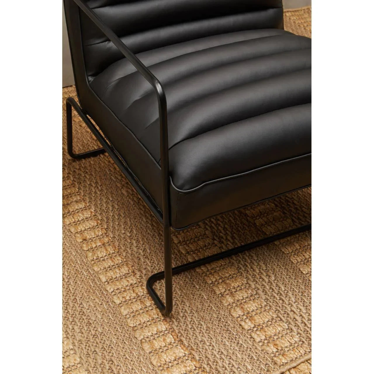 Black leather armchair with ribbed upholstery and metal frame on woven rug
