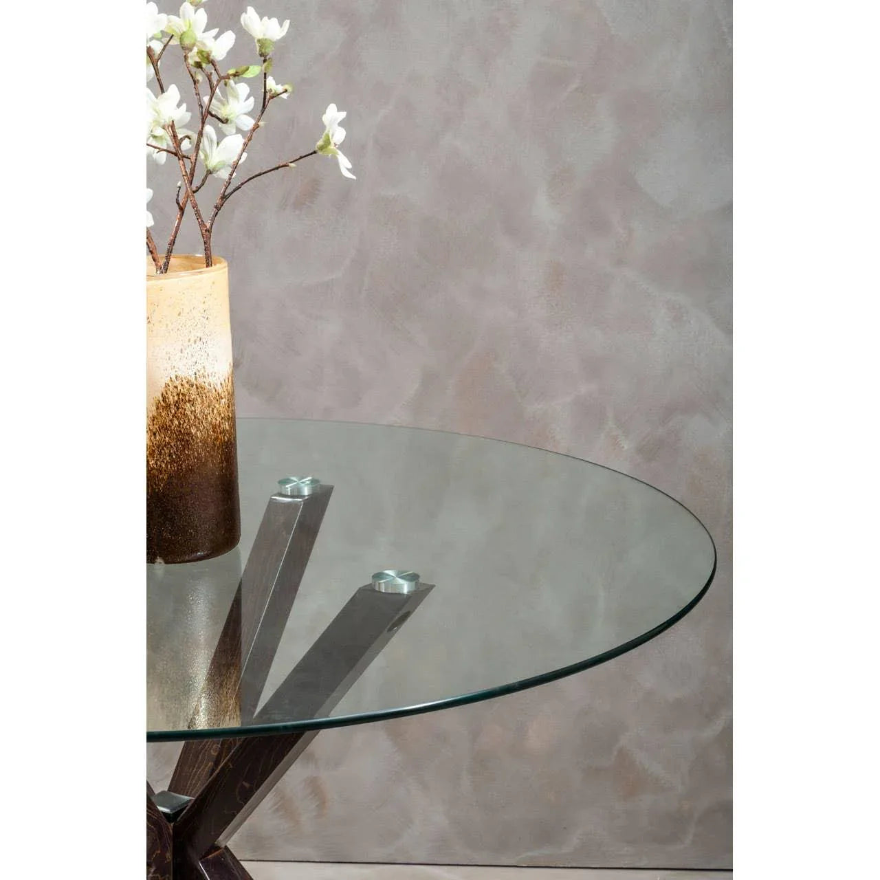 Round glass dining table with metal legs beside a ceramic flower vase