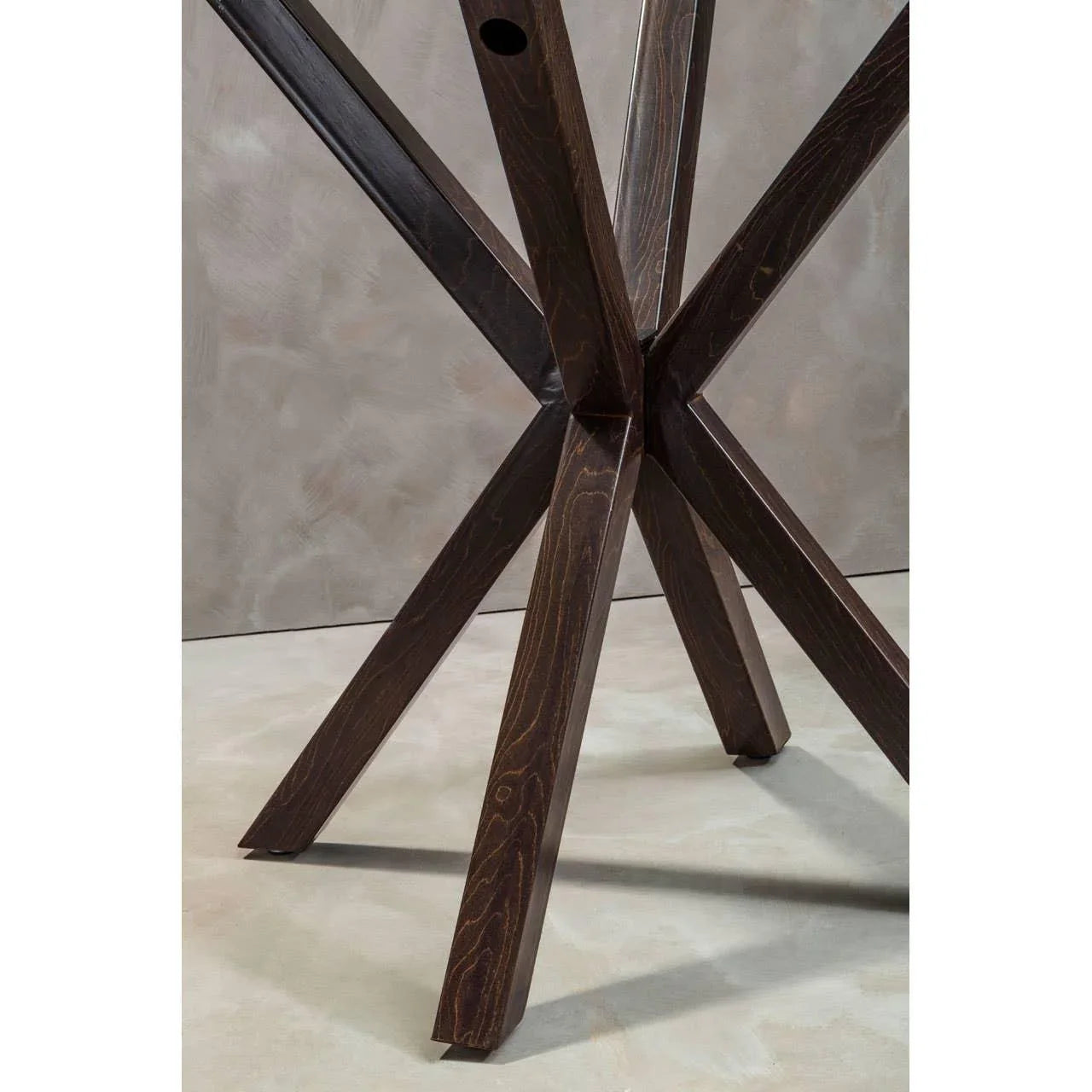 Dark wood dining table base with intersecting angled legs on neutral floor