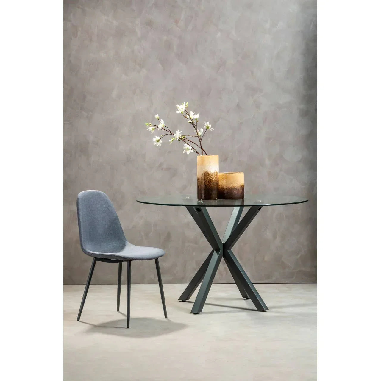Round glass dining table with black metal legs and single grey upholstered chair