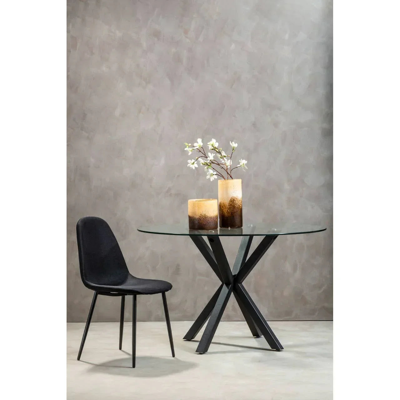 Round glass dining table with black metal legs and black chair, decorative vases on top