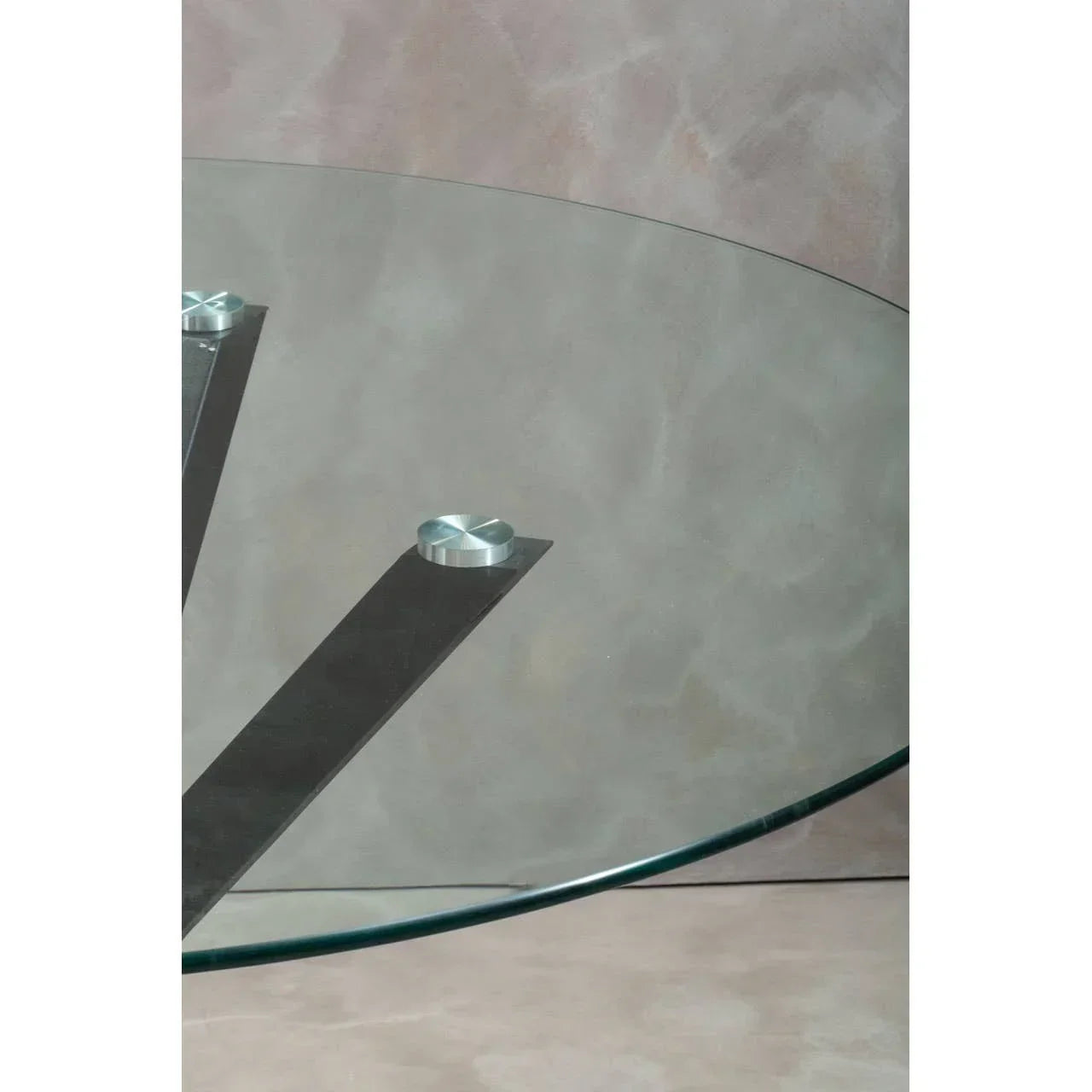 Glass dining table top with brushed metal legs against a neutral wall
