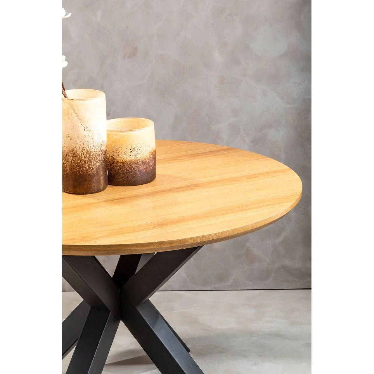 Round oak dining table with black metal legs and ceramic vases on top