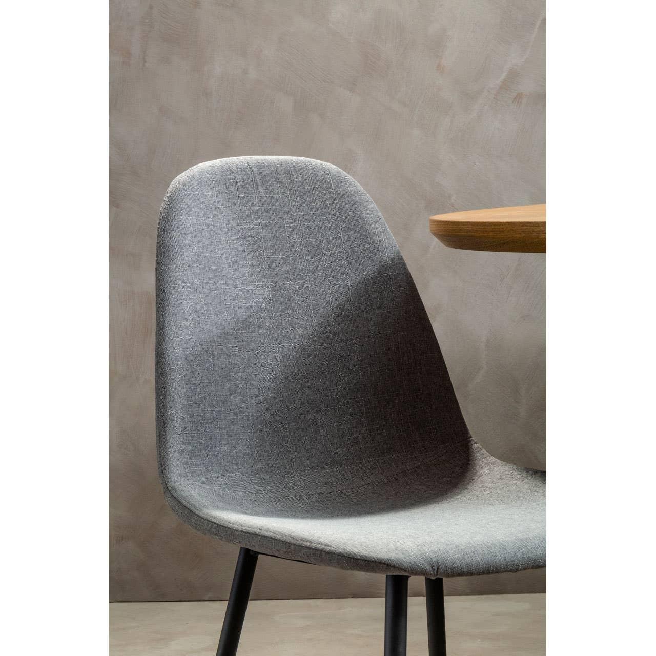Grey fabric dining chair with black legs beside round wooden table