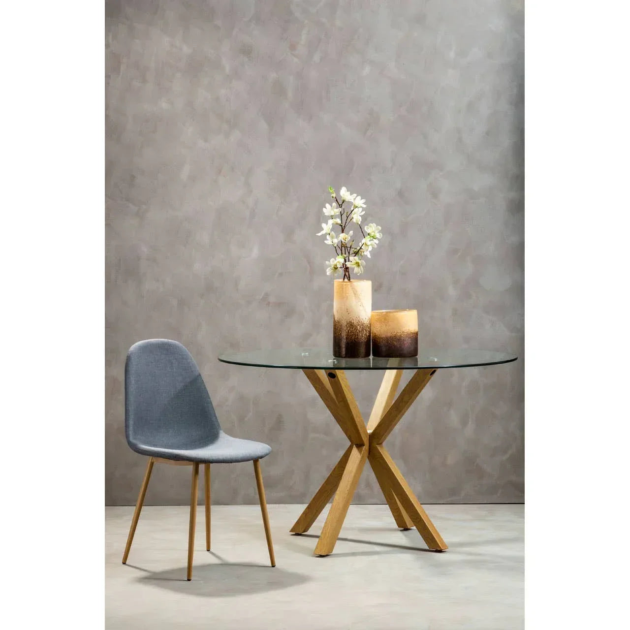 Round glass dining table with wooden legs, grey chair, vases and flowers on tabletop