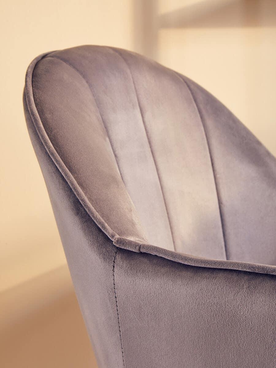 Close-up of grey velvet accent chair with curved backrest and stitched detail