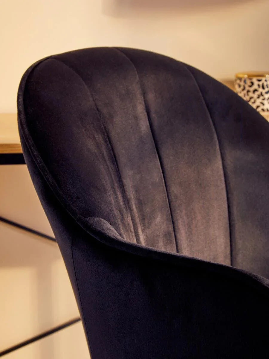 Black velvet accent chair with curved backrest beside wooden desk