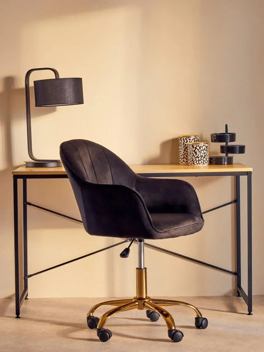 Black velvet office chair with gold base at wooden desk, featuring modern lamp and decor