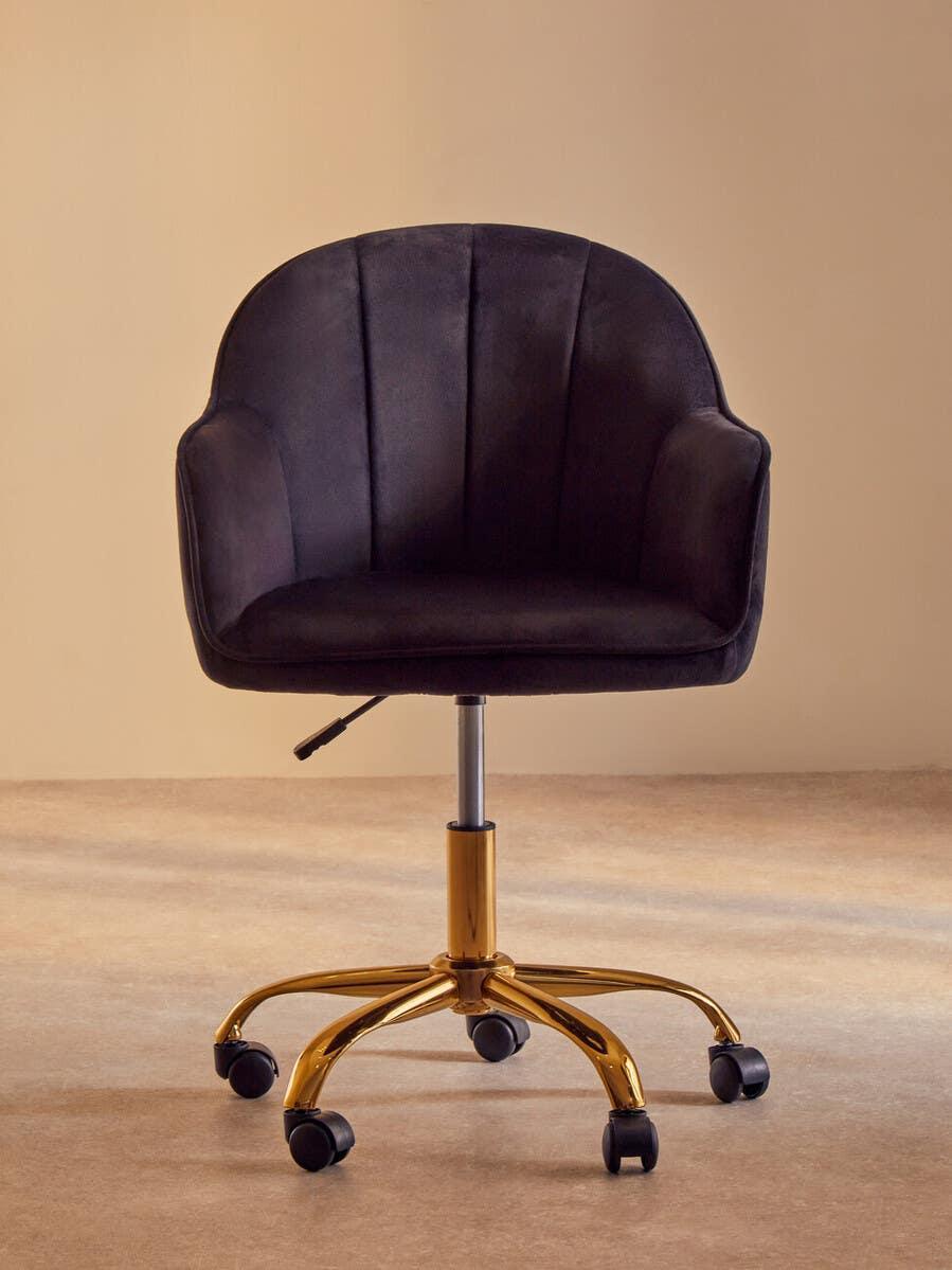 Black velvet office chair with gold metal base and rolling casters on neutral background