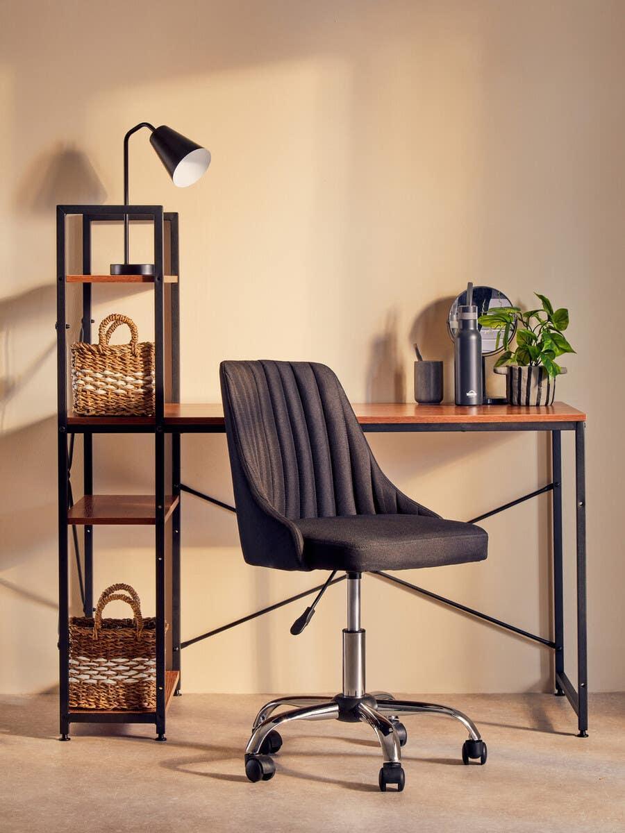 Contemporary black office chair at wood desk with shelving unit and desk lamp