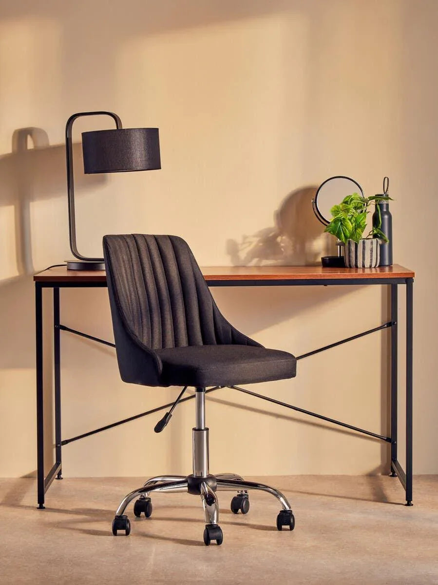 Black office chair with chrome base at wooden desk with lamp and plant