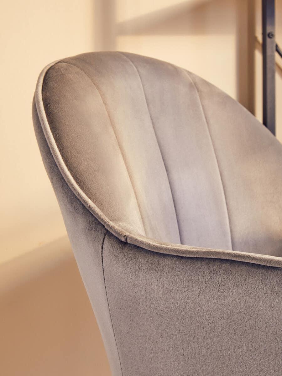 Close-up of grey velvet accent chair with curved backrest and stitched panel detail