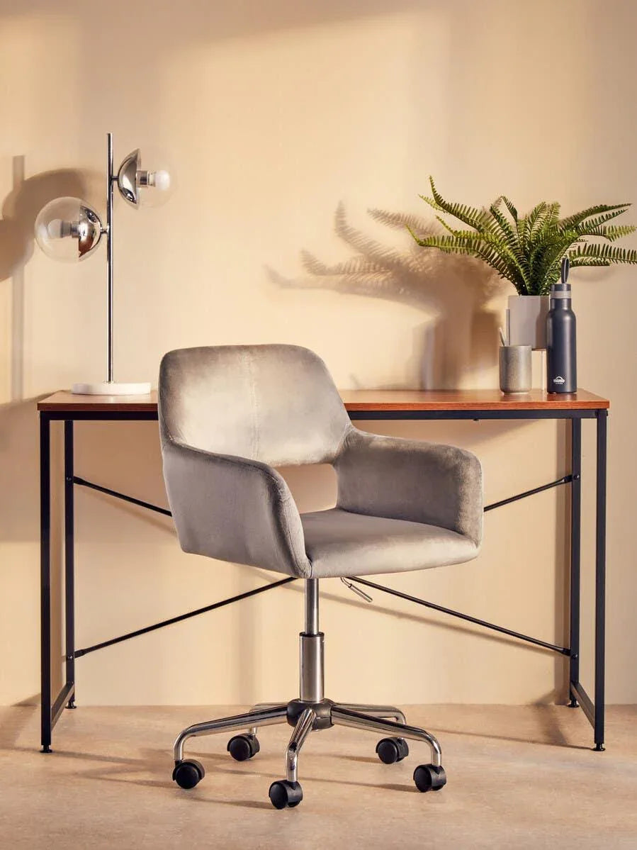 Grey office chair with chrome base at modern wooden desk, desk lamp and plant decor
