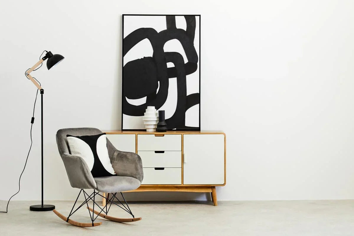 Modern grey rocking chair with cushion beside sideboard and abstract wall art