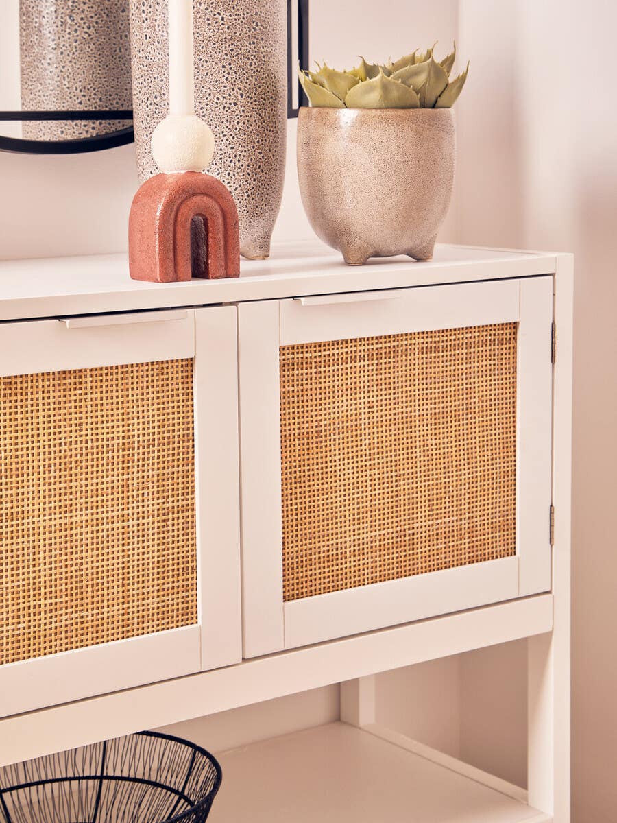 White wood side cabinet featuring two rattan front drawers, styled with a decorative vase and a small plant on top, against a neutral wall backdrop