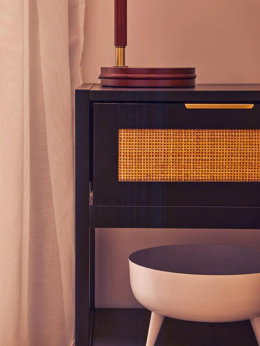 Black bedside table with woven rattan drawer front and white decorative bowl underneath