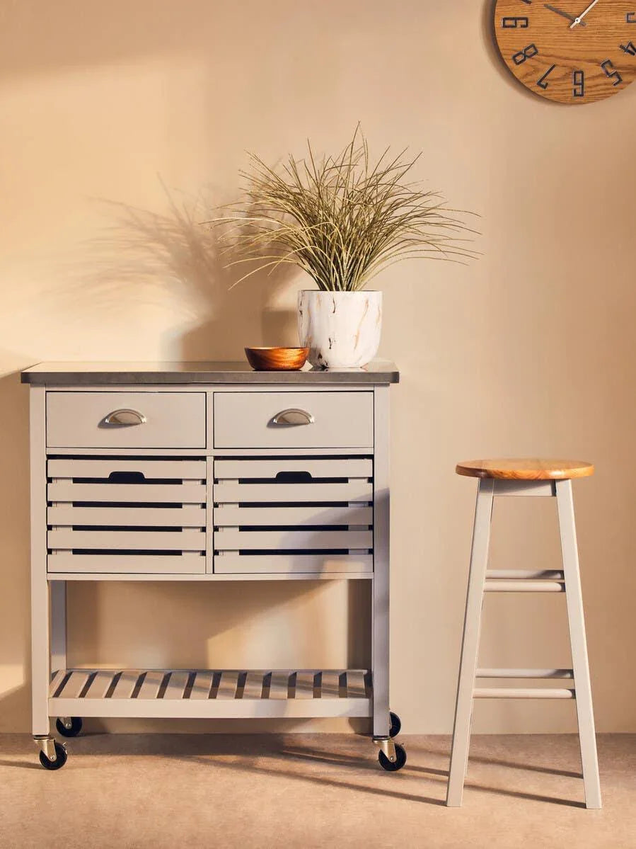 Grey kitchen trolley with drawers, potted plant, and wooden stool beside beige wall clock