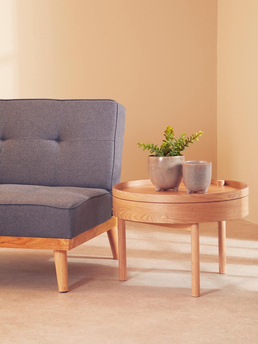 Grey fabric sofa with wooden frame beside round wooden side table holding two ceramic plant pots