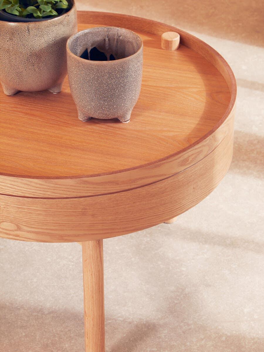 Round wooden coffee table with raised edge and two textured stone planters