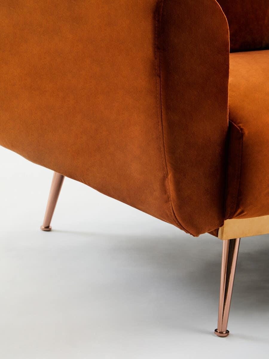 Brown velvet sofa armrest with gold metal legs, corner detail on light background