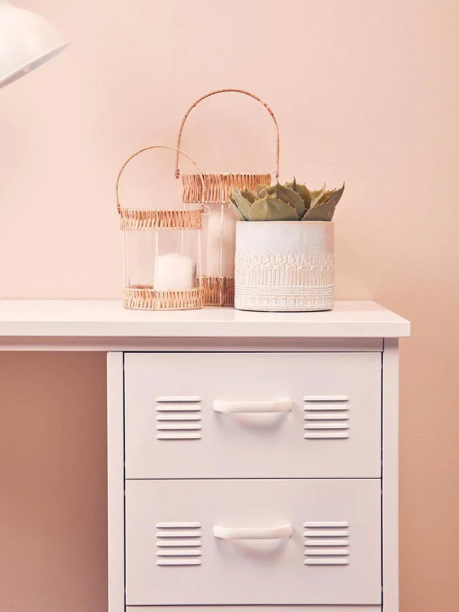 White storage cabinet with drawers, rattan candle holders and potted plant decor on top