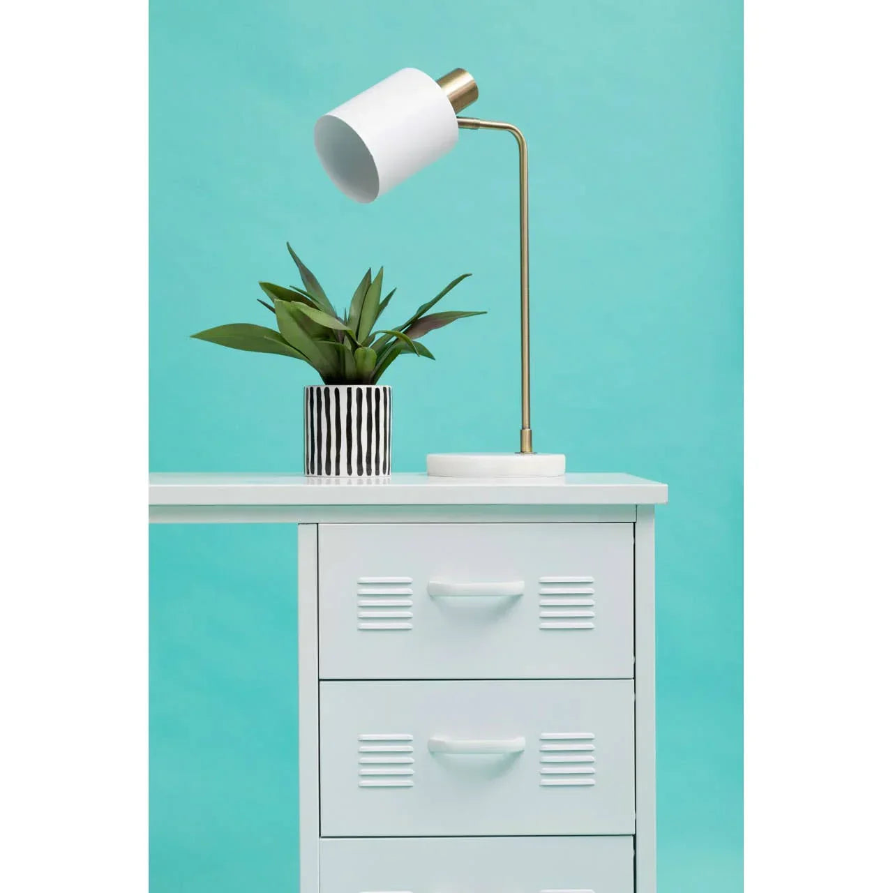 White metal bedside cabinet with drawers, gold desk lamp and potted plant on top