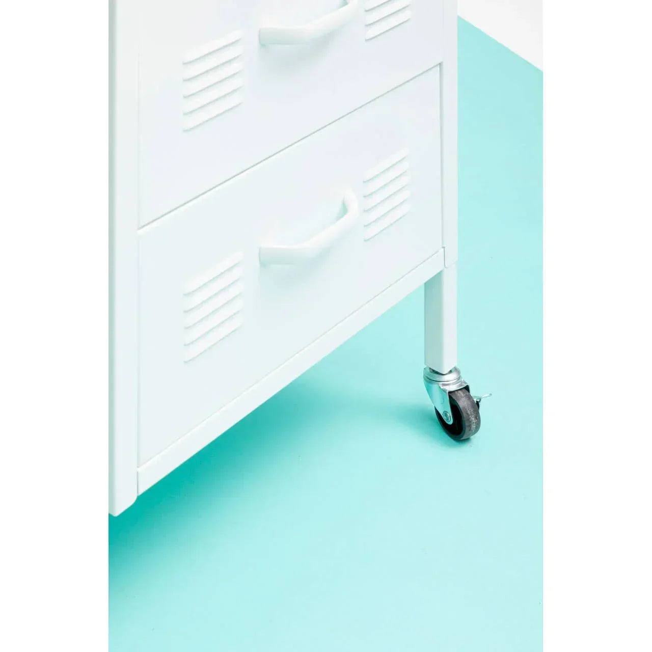White metal storage unit with drawers and caster wheel on turquoise floor