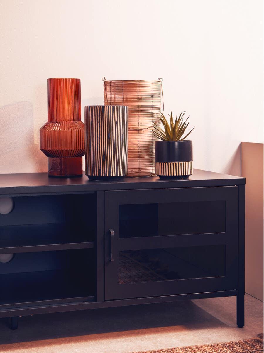 Black glass TV unit with decorative vases and plant arranged on top