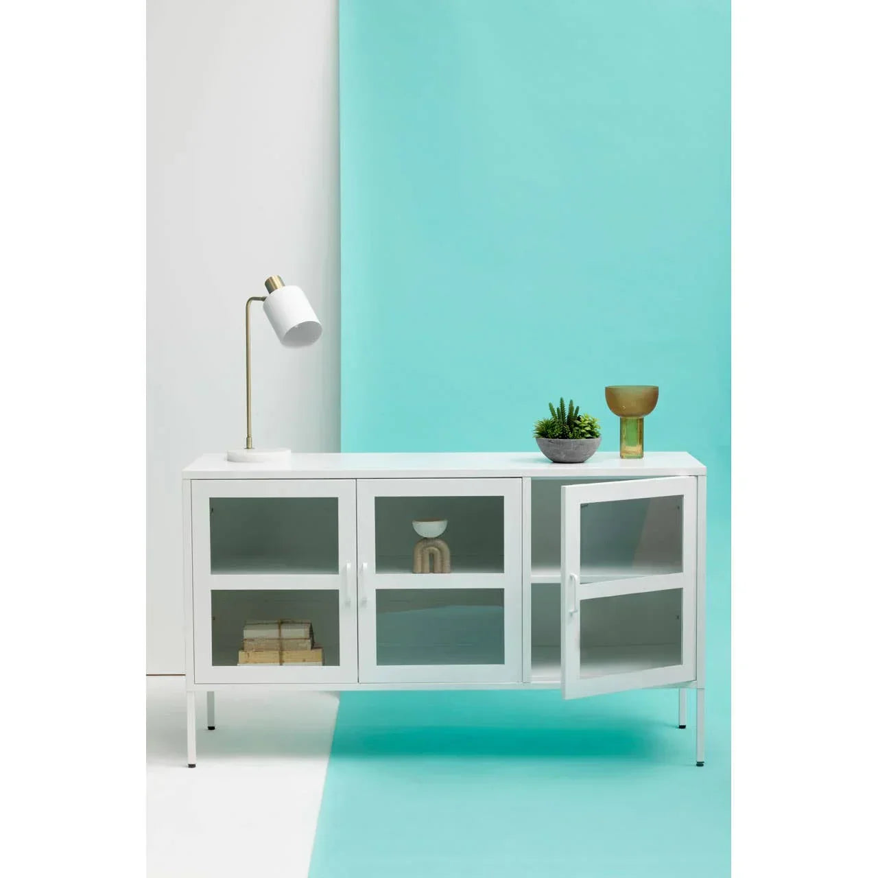 White sideboard cabinet with glass doors, lamp, plant and decor against blue wall