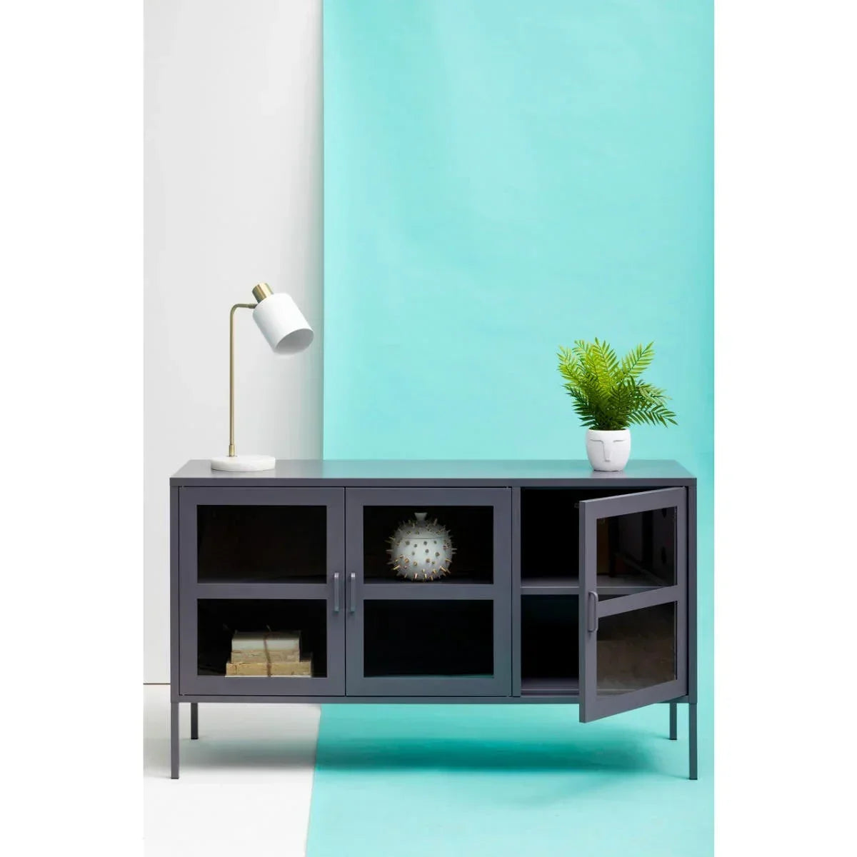 Grey metal sideboard with glass doors, gold desk lamp and potted plant on top